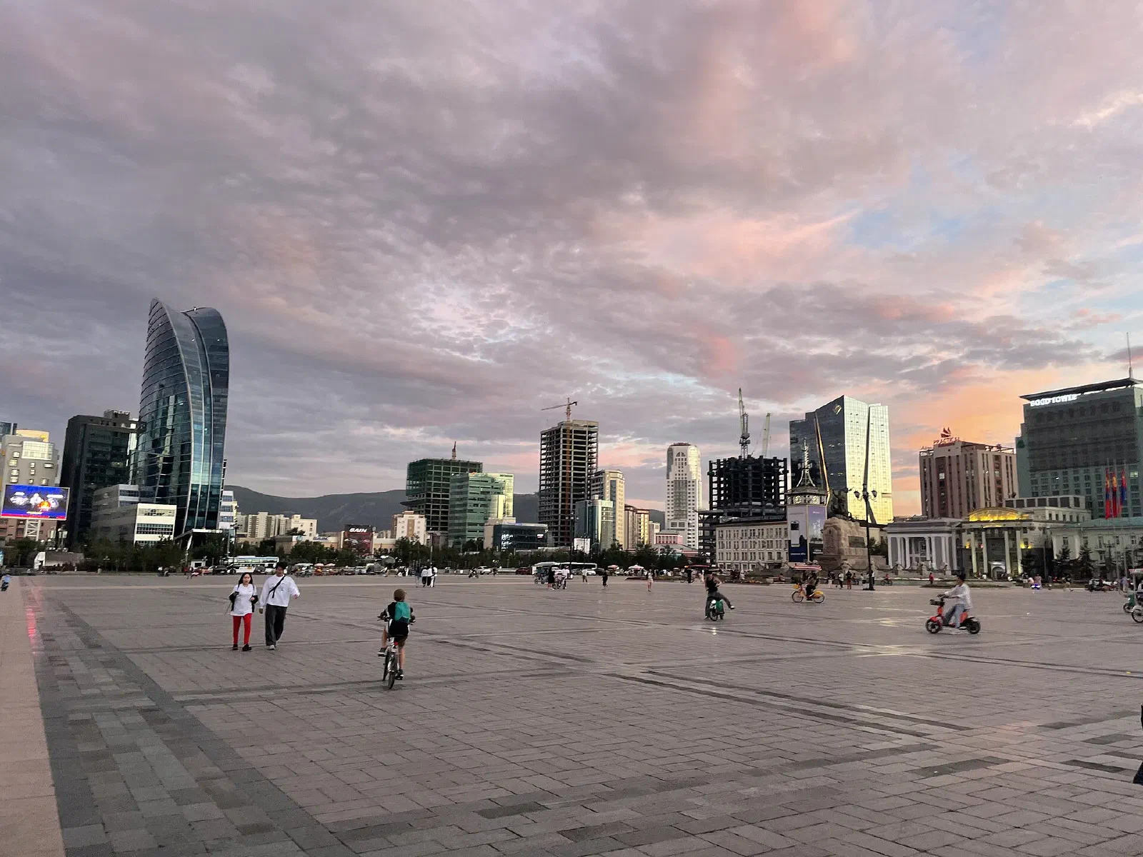 Улаанбаатар хотын төв: Сүхбаатарын талбай, ар талд Blue Sky цамхаг болон өндөр барилгууд, үдшийн ягаавтар тэнгэр