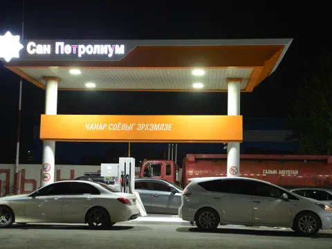 Шөнийн цагаар гэрэлтсэн «Сан Петролиум» бичигтэй ШТС-ын саравчны доор зогсож буй суудлын машинууд, ар талд улаан өнгийн шатахууны цистерн машин