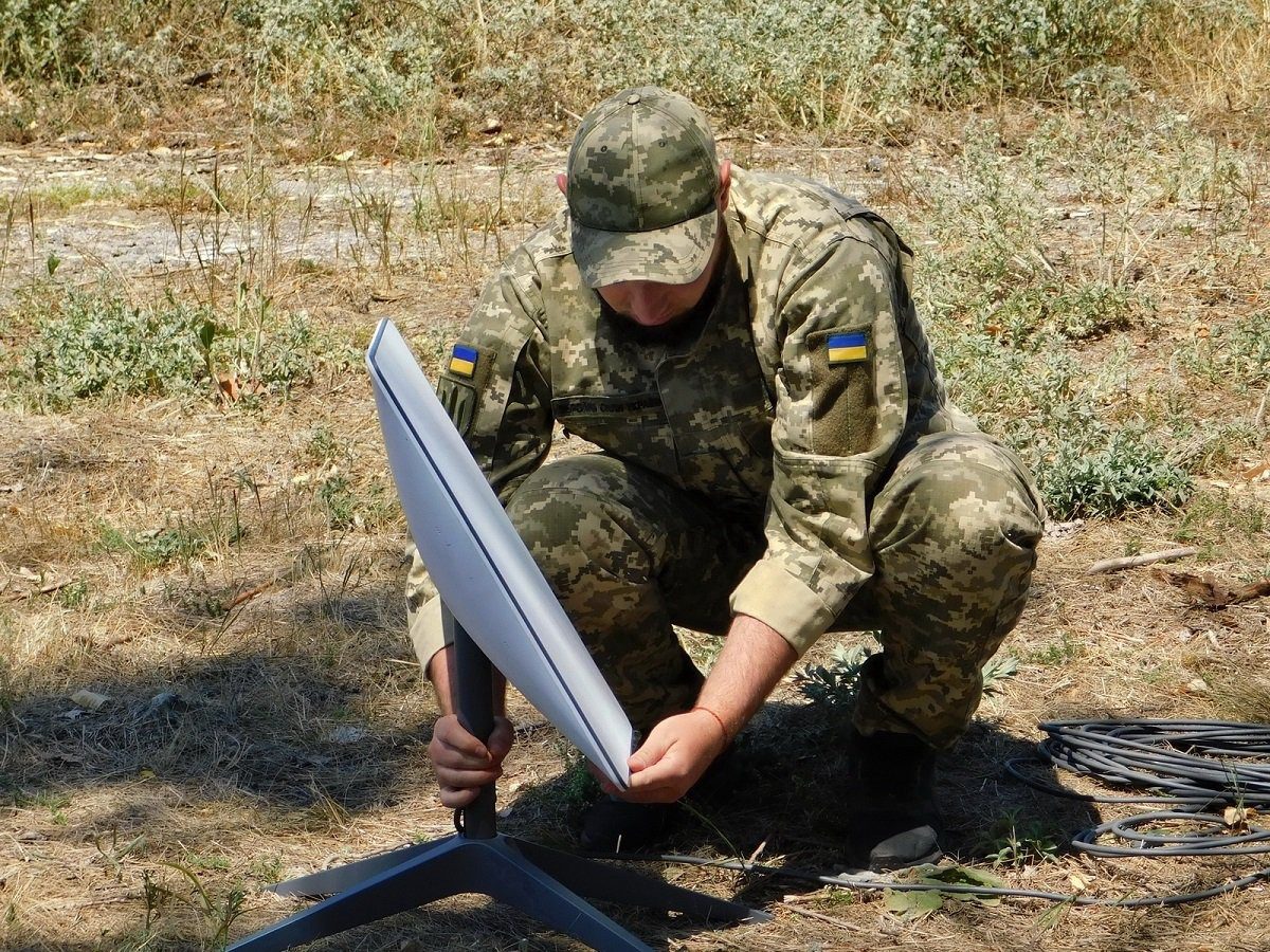 Украины далбаатай цэргийн хувцастай цэрэг хээр газар цагаан хавтгай Starlink антенныг тавиур дээр суурилуулж байна
